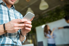 Closeup of hands of young man in checkered shirt using mobile phone while his partners arguing-1